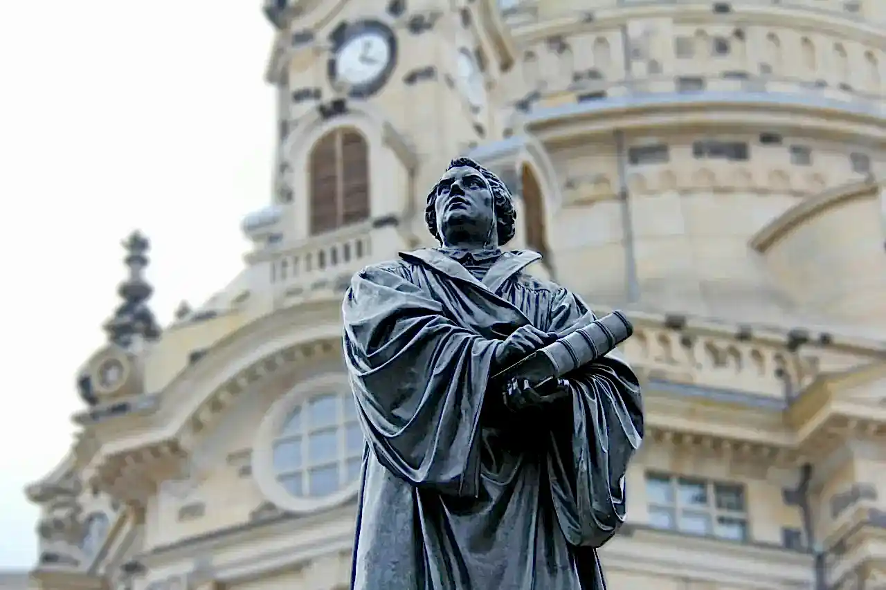 gray concrete statue of man holding book beside brown building